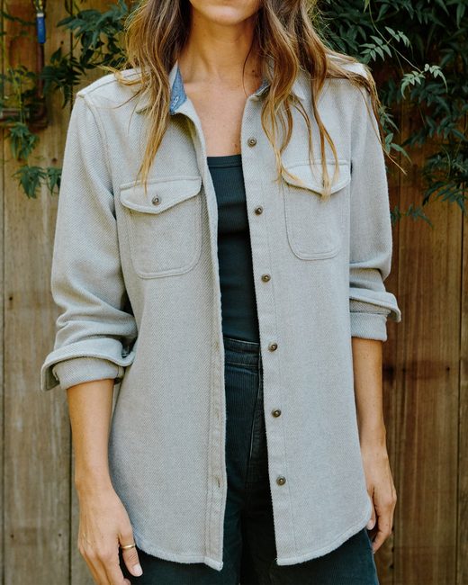 A person wearing a light gray button-down shirt over a dark tank top and dark pants.