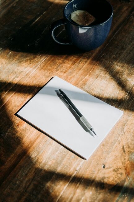 A mechanical pencil rests on a blank notepad ready for brainstorming, placed next to a mug of tea on a wooden table.