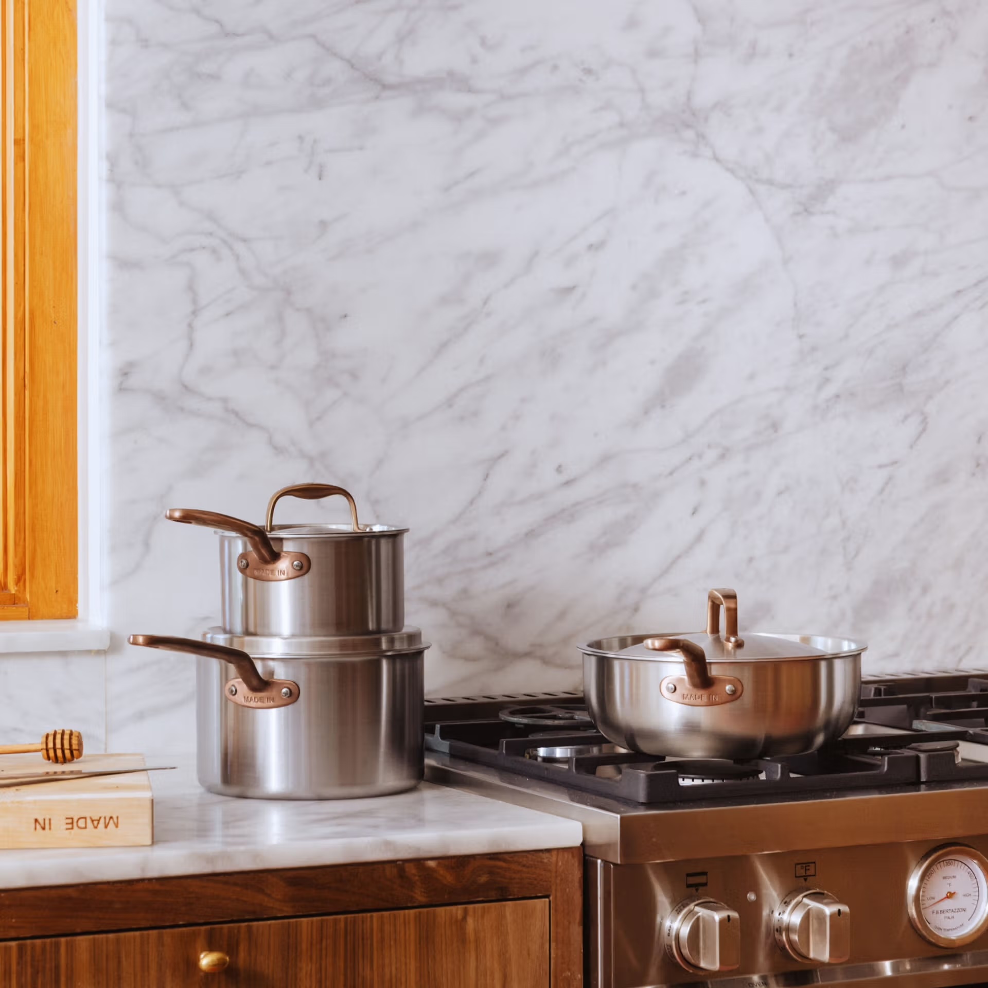 Two stainless steel saucepans stacked on a marble countertop next to a sauté pan on a gas stovetop.