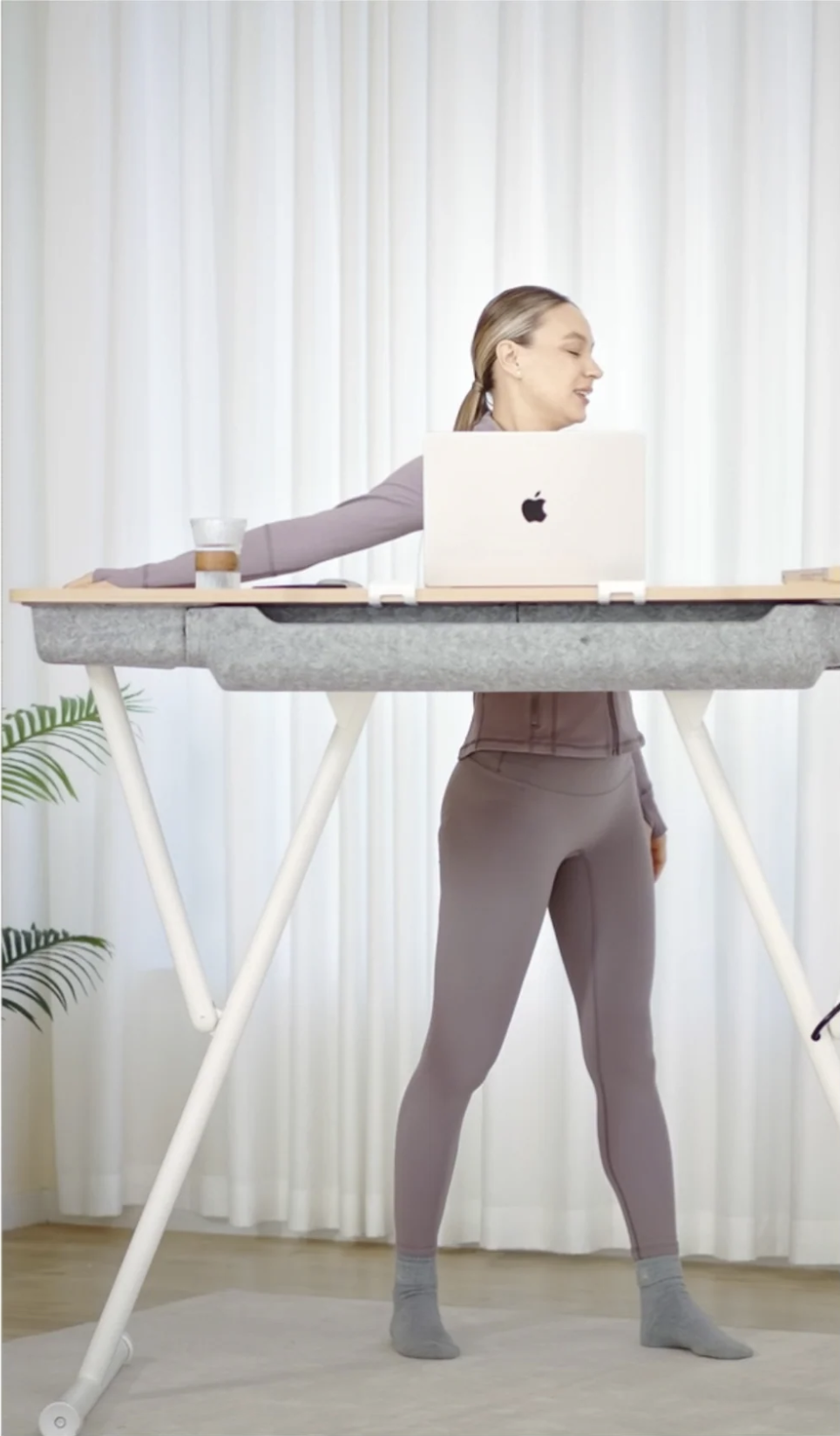 A person in athletic wear standing at a height-adjustable desk with a laptop.