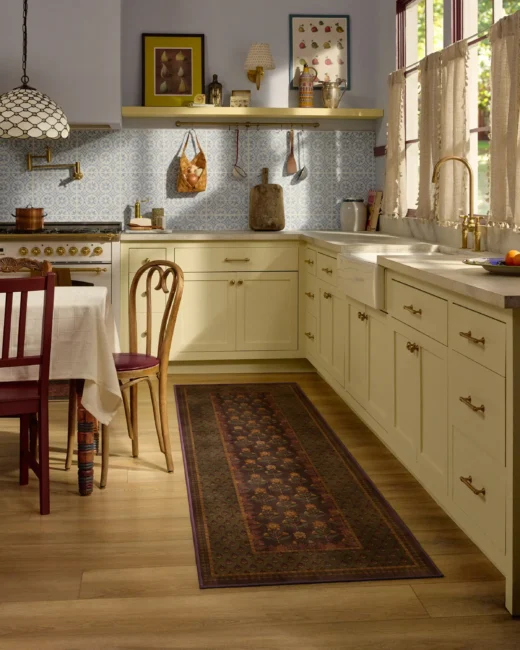 Cream-colored kitchen cabinets with a floral runner rug, a farmhouse sink, and a dining table with chairs.