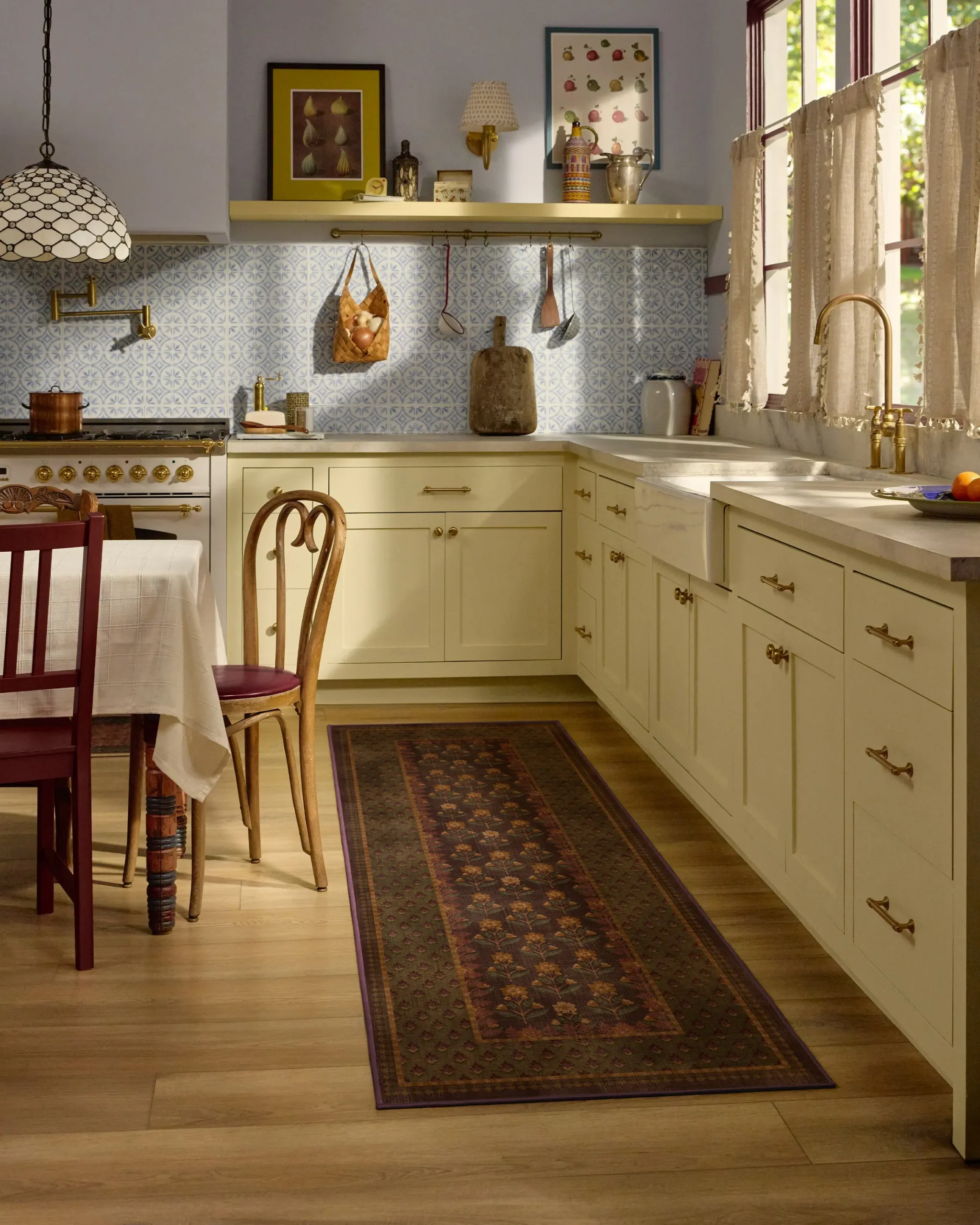 Cream-colored kitchen cabinets with a floral runner rug, a farmhouse sink, and a dining table with chairs.